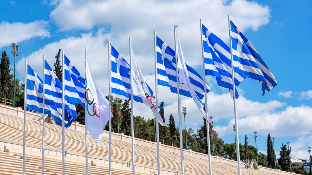 Greek flags waving at Panathenaic Stadium under a clear sky, reflecting Olympic spirit.