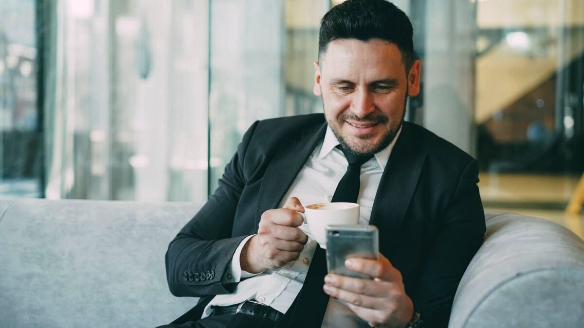 A man in a suit checks news on his phone while drinking coffee