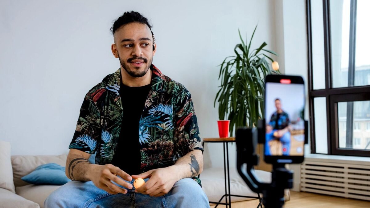 A young man records a video indoors with a camera on a tripod and a microphone