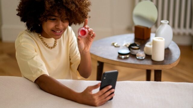 A young woman films a review of beauty products on a phone fixed to a tripod.