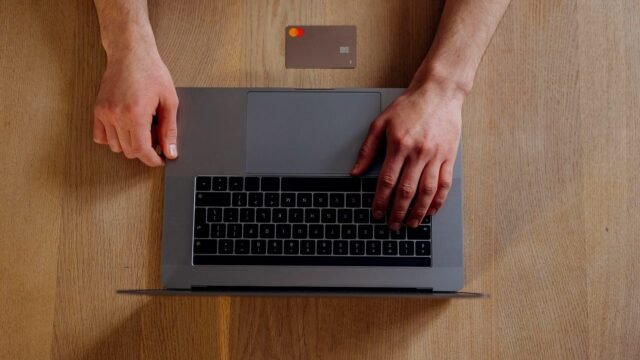 Hands at a laptop holding a payment card during an online purchase