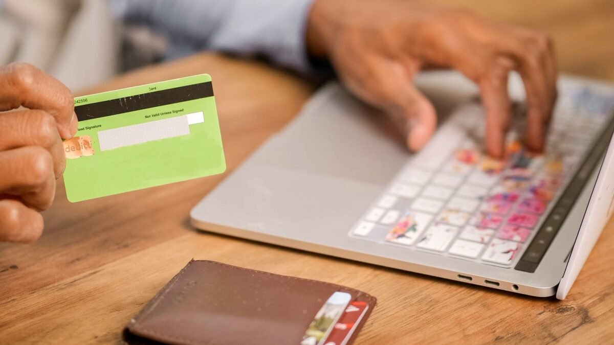 Hands at a laptop holding a payment card while placing an order in an online shop