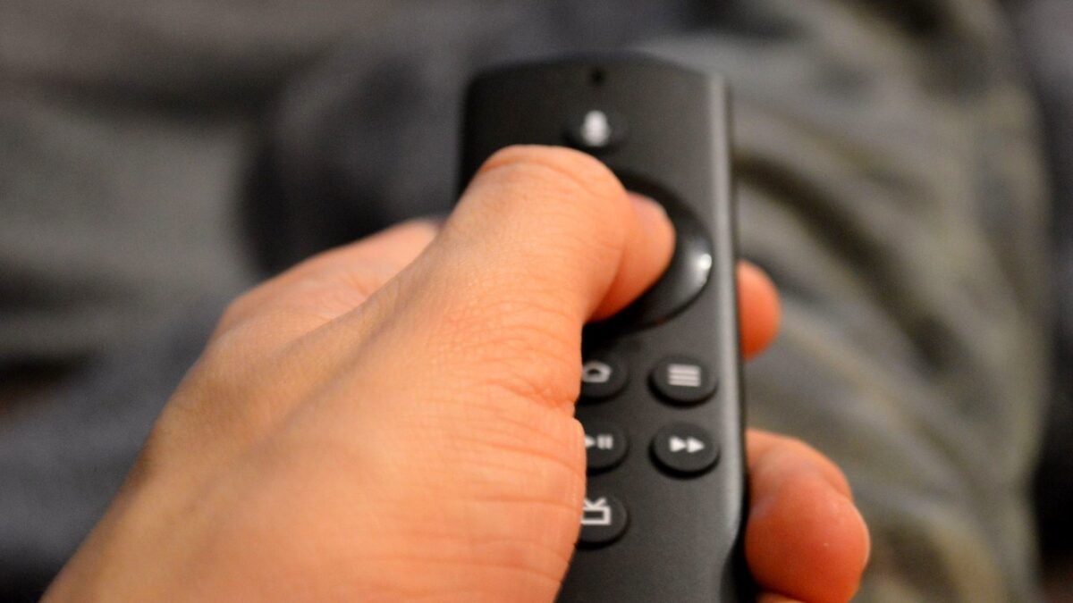 A viewer’s hand on a TV remote control, shot close up.