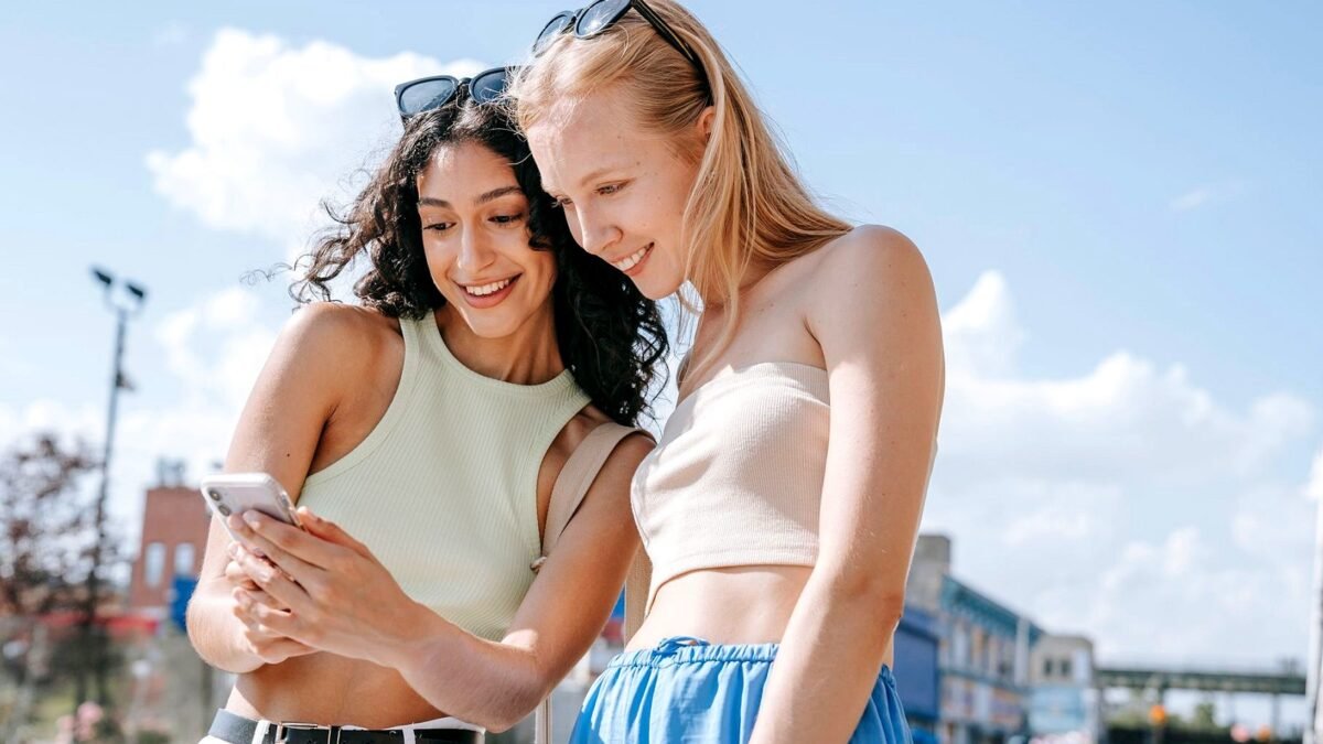 Two women standing outdoors and looking together at a smartphone screen