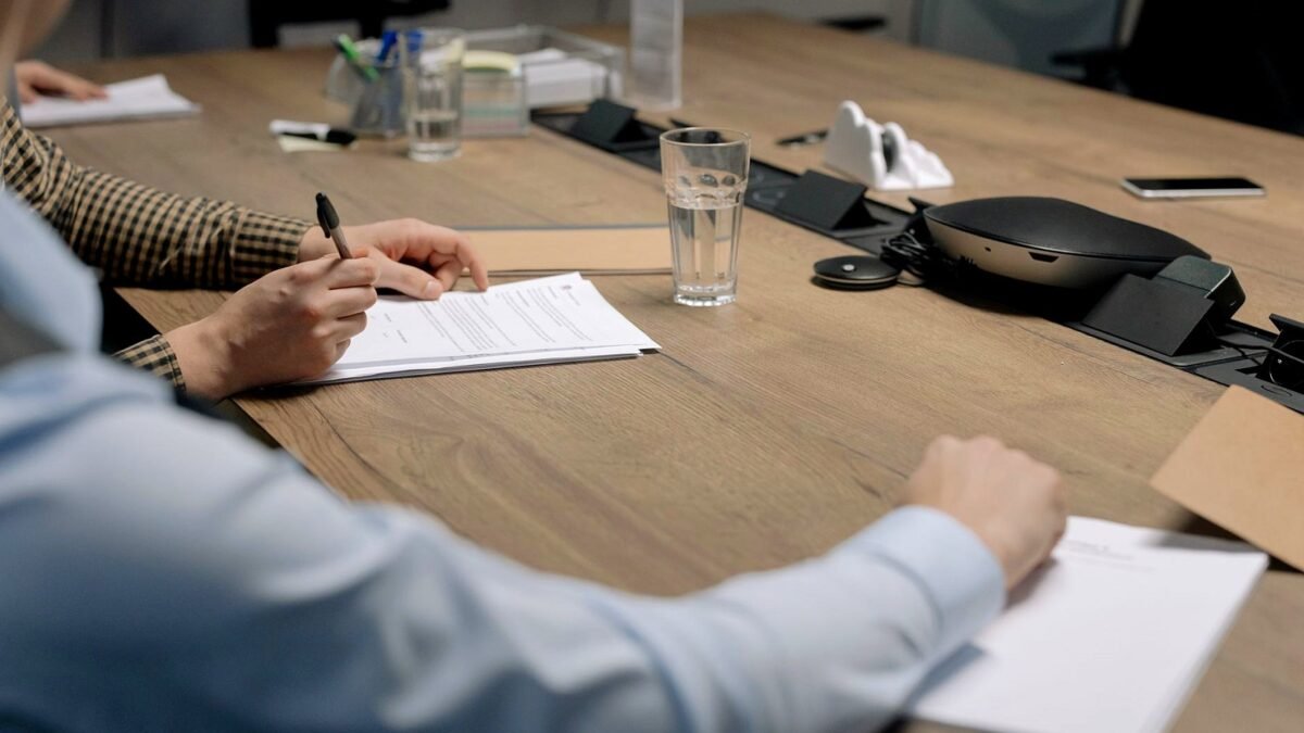 Hands resting on printed documents during a board meeting at a wooden table