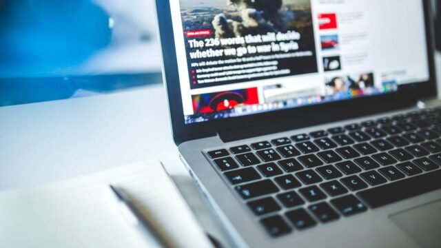 An open laptop on a desk shows an online news article with a large headline.