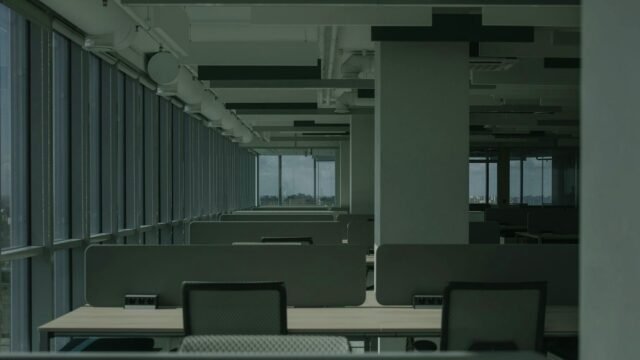 Rows of empty desks in a bright open-plan office with large windows