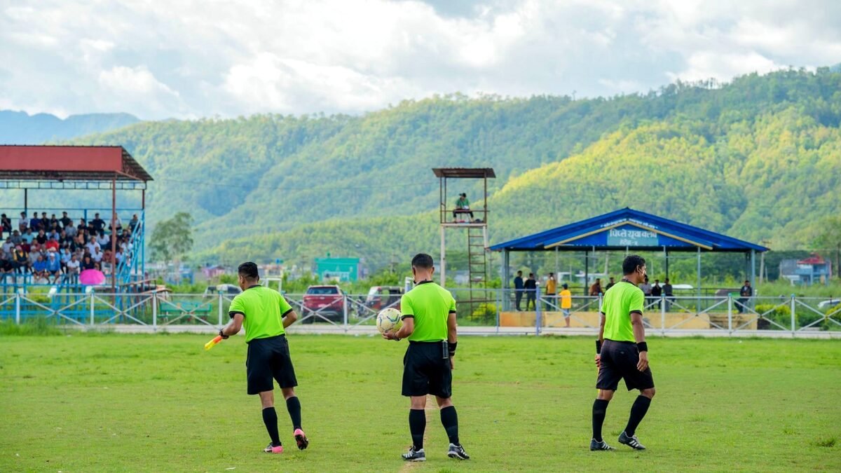 Three football referees in green kit on the pitch during a daytime match