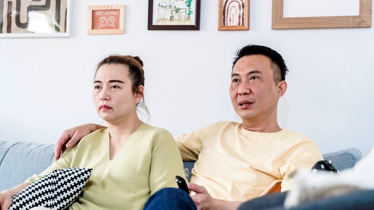 Two people watch television from a sofa in a living room.