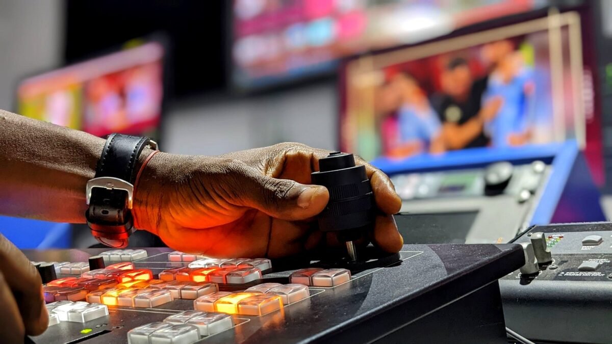 A hand moves faders on a broadcast mixing desk in a television control room