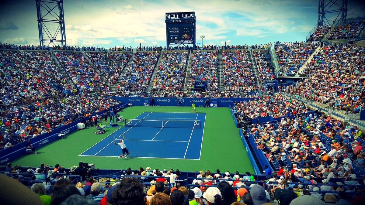 A packed stadium watches a tennis match on a blue hard court at the US Open.
