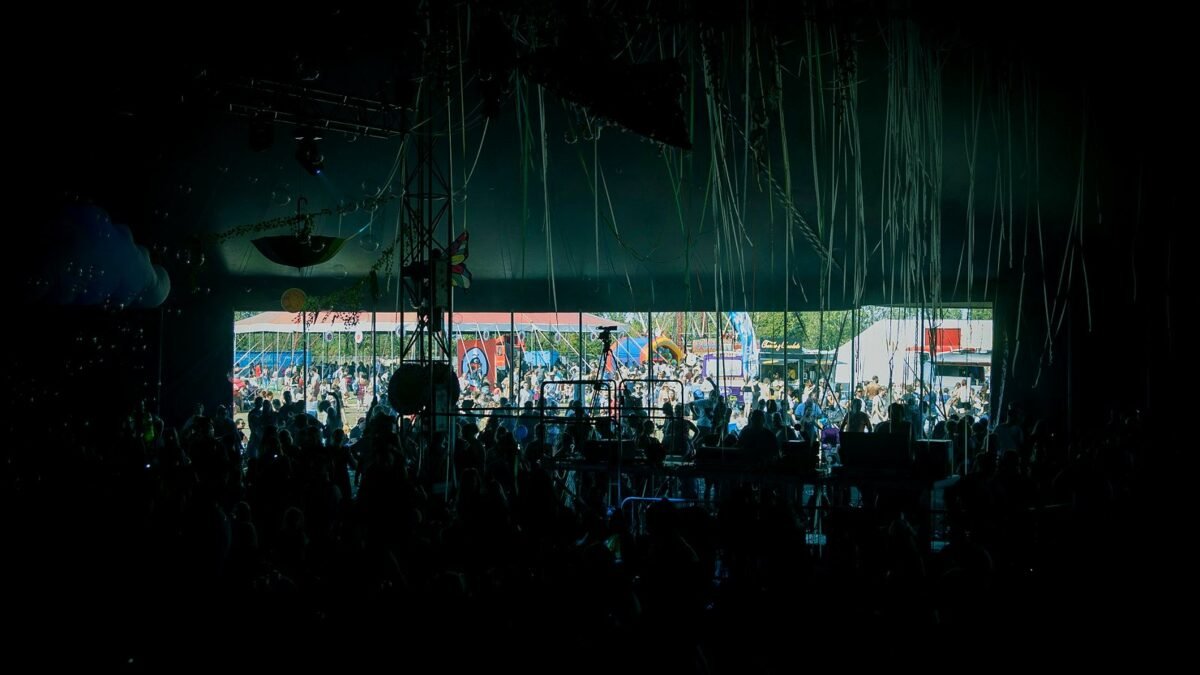 A daytime festival crowd with raised hands in front of an outdoor stage.