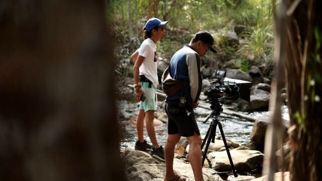 Two filmmakers set up a camera on a tripod before a documentary shoot.