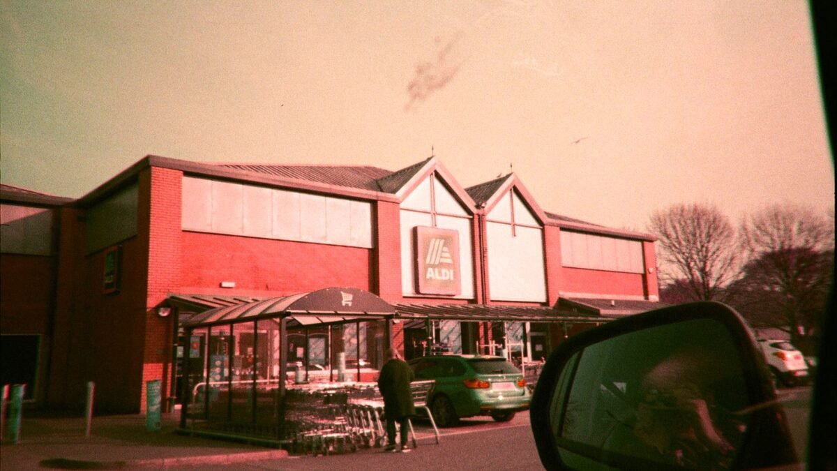 An Aldi supermarket with parked cars, seen in a car side mirror