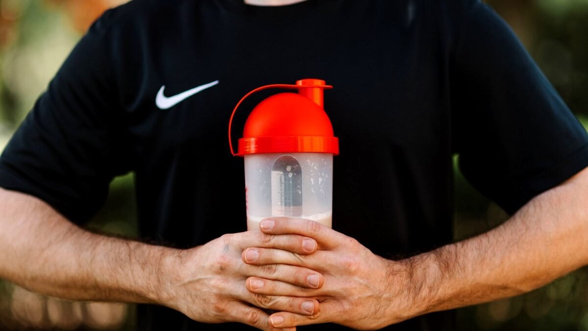 Hand holding a protein shaker with a red lid outdoors