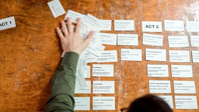 Hands arranging storyboard cards on a wooden table during campaign planning
