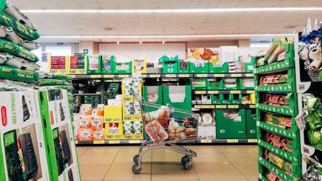 A shopping cart standing in a brightly lit supermarket aisle
