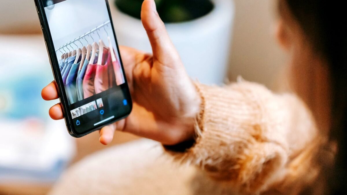 A person in casual clothes scrolls through photos of outfits on a phone, face out of frame