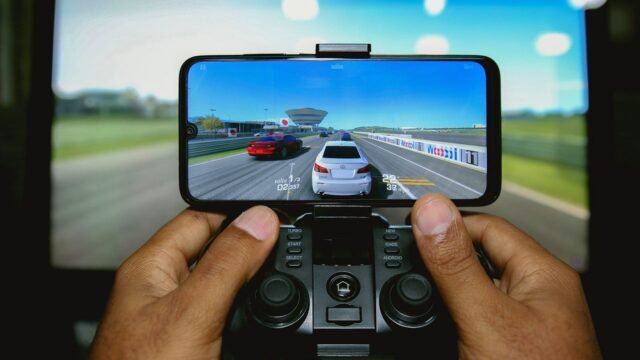 Hands holding a phone clipped to a game controller during a racing game