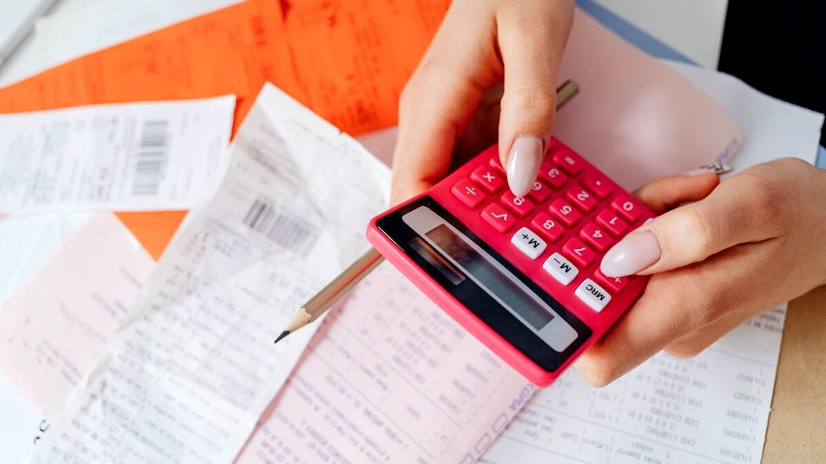 Hands with a calculator checking a pile of receipts and bills on a desk