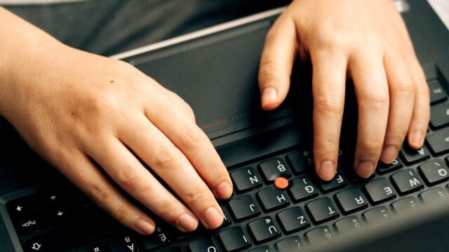 Hands typing on a black laptop keyboard at a desk