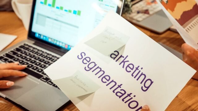 Hands point at marketing charts on a laptop screen next to printed reports