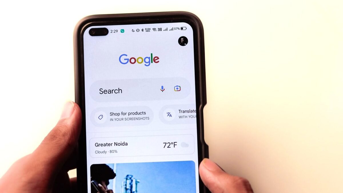 A hand holds a phone with the Google search page open on the screen