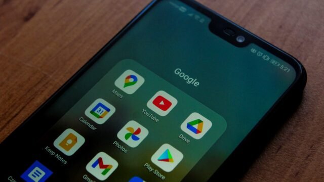 Hand holding a smartphone with a folder of Google apps open on the screen