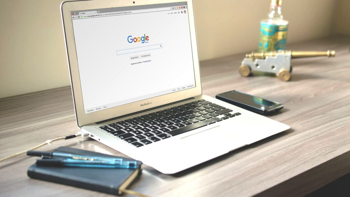 Laptop on a desk with the Google search page open, next to a smartphone and a notebook
