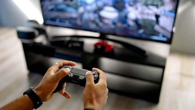 Hands hold a game controller in front of a TV screen during a video game session