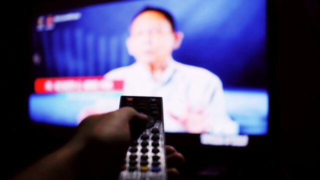 Hand holding a remote control aimed at a television screen