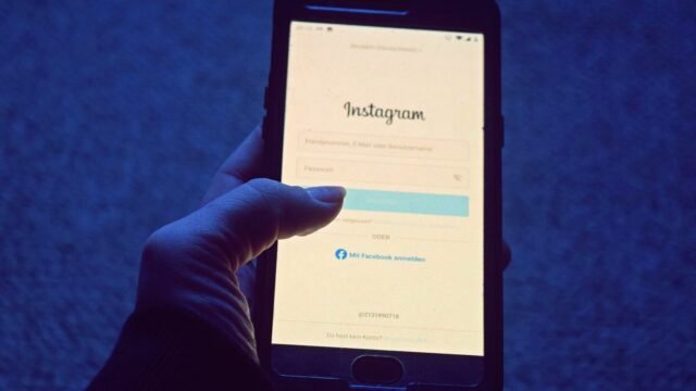 A hand holds a smartphone showing the Instagram login screen