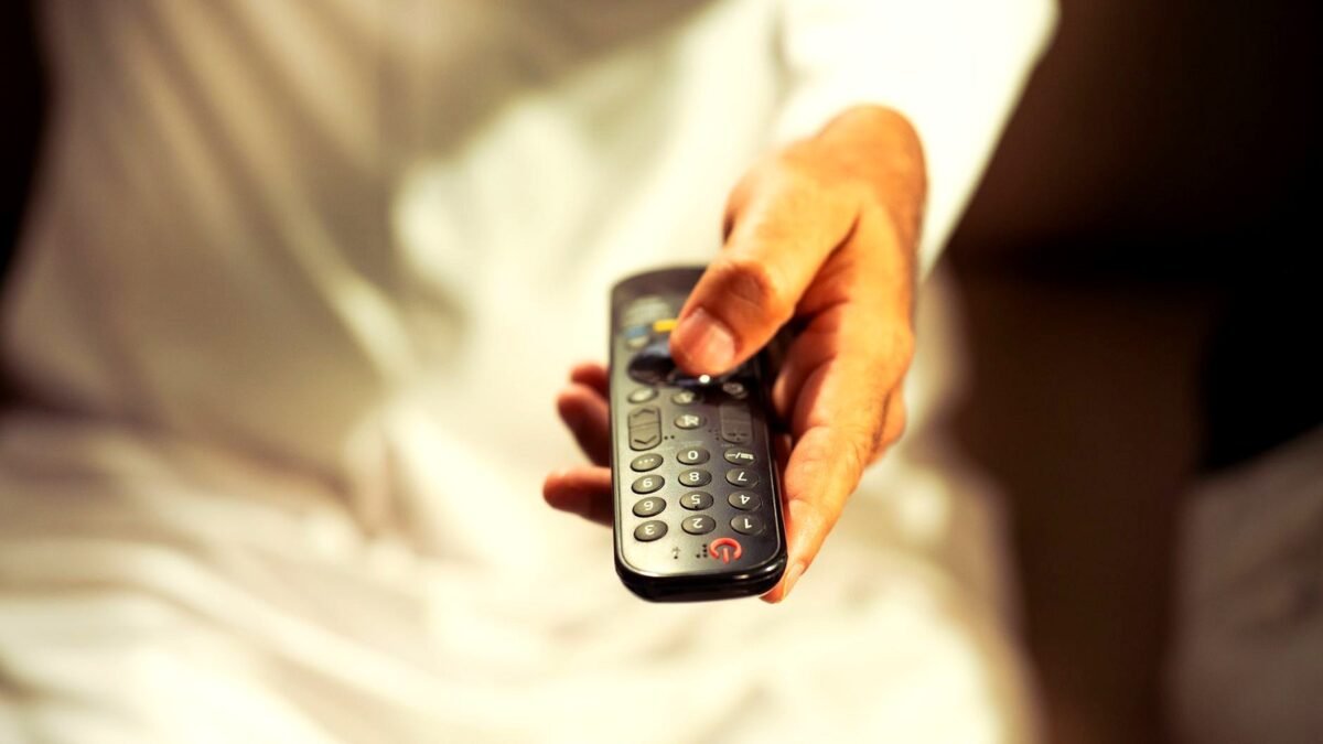 A hand holds a TV remote control pointed at a television screen