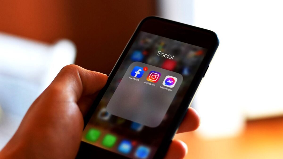 A hand holds a smartphone with the Facebook and Instagram app icons on the home screen