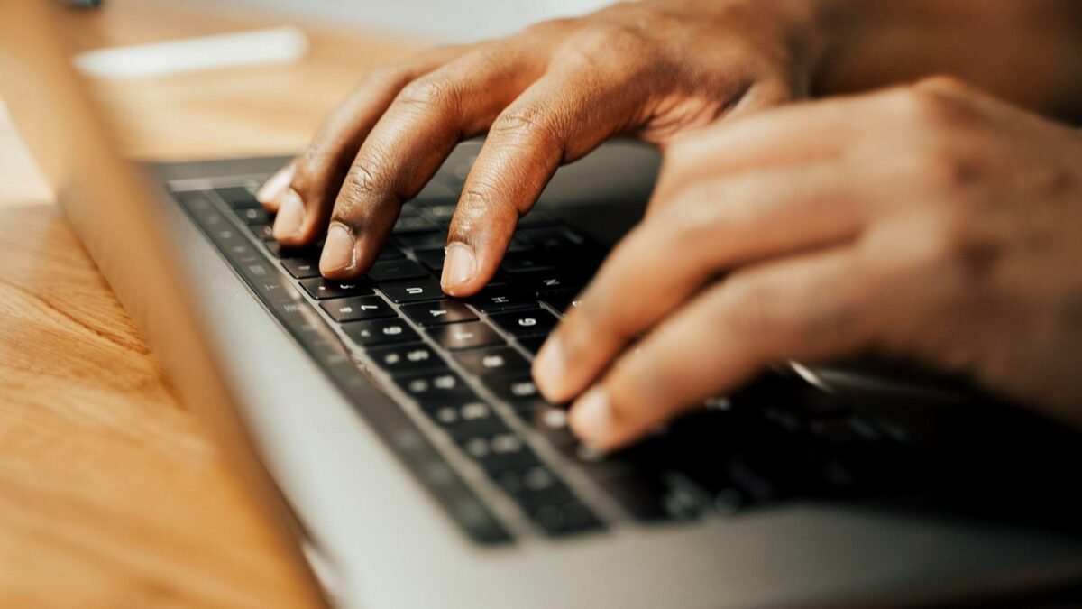 Hands typing on a laptop keyboard on a wooden desk