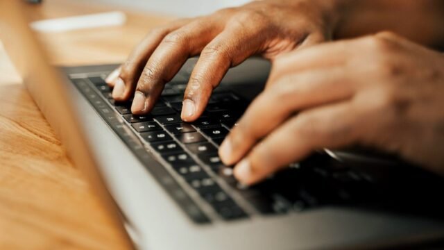 Hands typing on a laptop keyboard on a wooden desk