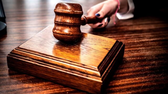 A hand holds a wooden gavel above a desk in a courtroom