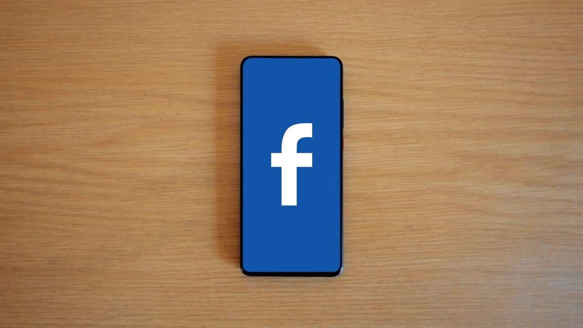 A smartphone with the Facebook logo on its screen lies on a wooden table