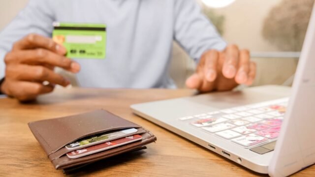 Hands holding a bank card next to a laptop during an online purchase
