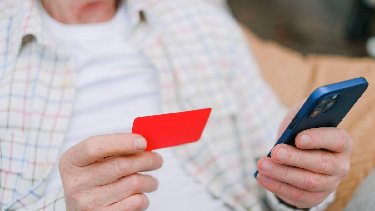 An older person holds a bank card and a smartphone at home