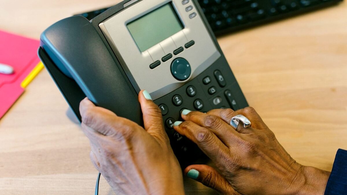 A hand dialling a desk telephone in an office