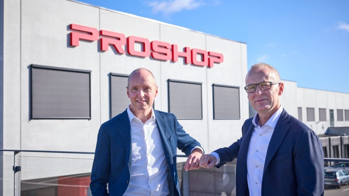 Two men in suits stand outside a building with a large red Proshop sign