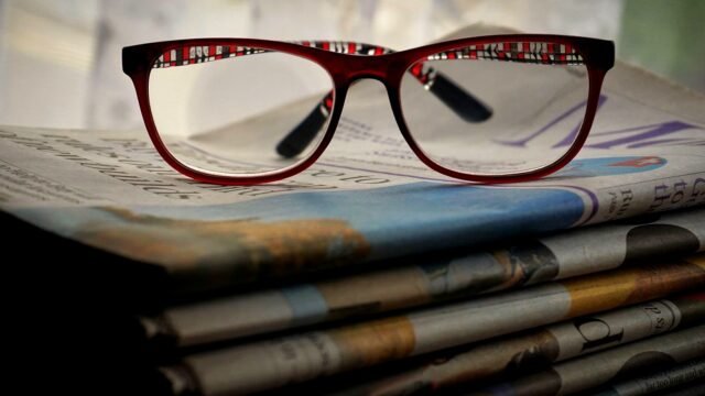Red reading glasses resting on a stack of printed newspapers