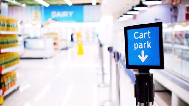 Digital screen on a stand in a bright supermarket aisle next to the dairy section