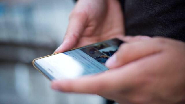 Close-up of two hands holding a smartphone and scrolling on its touchscreen.