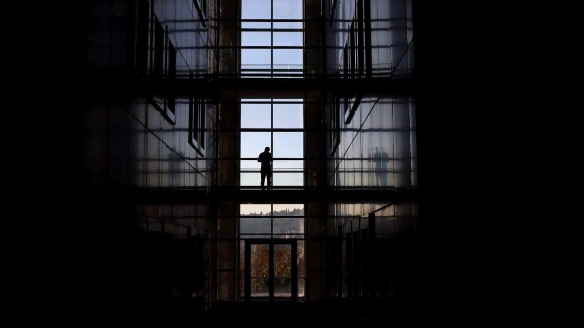 Silhouette of a person standing in a glass atrium with city buildings behind