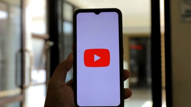 Hand holding a phone with the YouTube app open on the screen